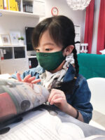 A little girl who wears a green reusable mask is reading a book